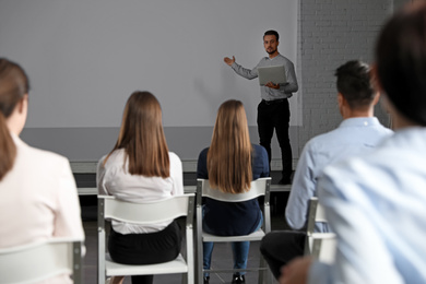 Male business trainer with laptop giving lecture in conference room with projection screen