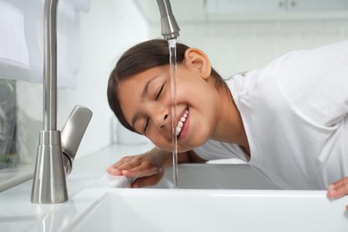 Girl drinking tap water over sink in kitchen