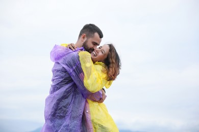 Young couple in raincoats enjoying time together under rain outdoors, space for text