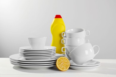 Photo of Clean tableware, dish detergent and half of lemon on white wooden table against light background