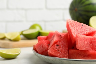 Photo of Slices of delicious watermelon and limes on white wooden table, closeup. Space for text