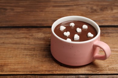 Photo of Cup of hot chocolate with heart shaped marshmallows on wooden table, space for text