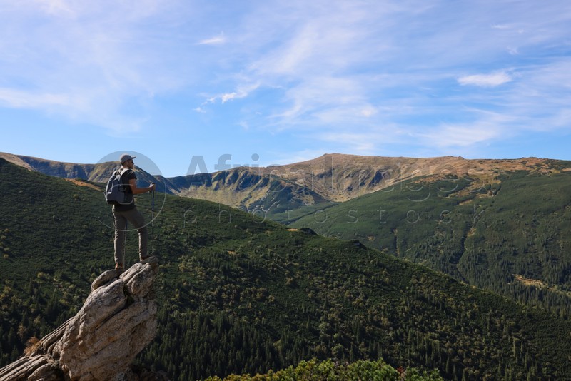 Man with trekking poles enjoying picturesque view on cliff in mountains. Space for text