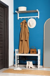 Photo of Stylish hallway with shoe storage bench and mirror near blue wall. Interior design