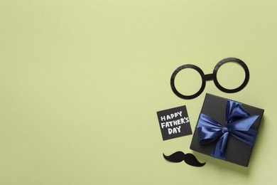 Photo of Card with phrase HAPPY FATHER'S DAY, paper glasses, mustache and gift box on light green background, flat lay. Space for text