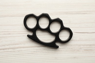 Black brass knuckles on white wooden background, top view
