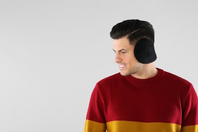 Man wearing stylish earmuffs on light background. Space for text