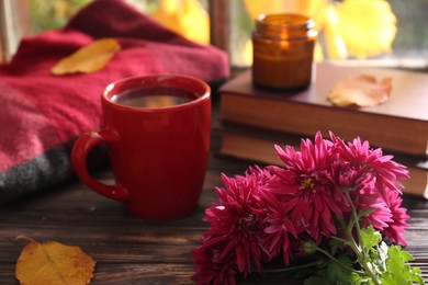 Beautiful chrysanthemum flowers, cup of hot drink and books on wooden table. Autumn still life