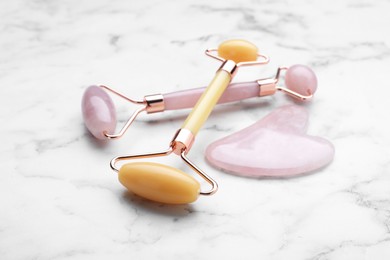 Photo of Gua sha stone and different face rollers on white marble table