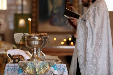 MYKOLAIV, UKRAINE - FEBRUARY 27, 2021: Priest conducting baptism ceremony in Kasperovskaya icon of Mother of God cathedral, focus on vessel with holy water and brush