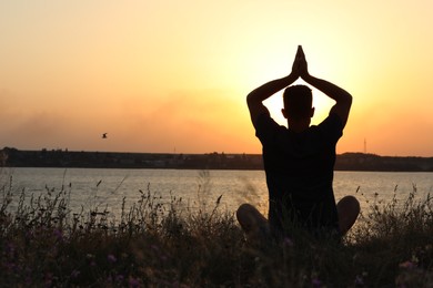 Photo of Man meditating near river at sunset, back view. Space for text