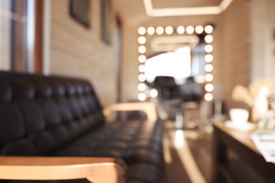 Photo of Blurred view of stylish barbershop interior with leather sofa and large mirror