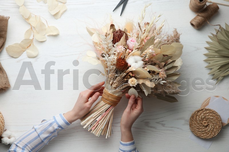 Florist making beautiful bouquet of dried flowers at white table, top view