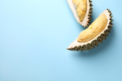 Pieces of fresh ripe durian on light blue background, flat lay. Space for text