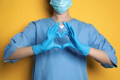 Doctor making heart with hands on yellow background, closeup