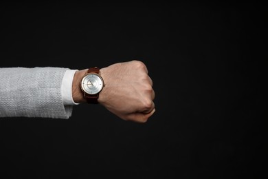 Businessman wearing wristwatch on black background, closeup. Time management