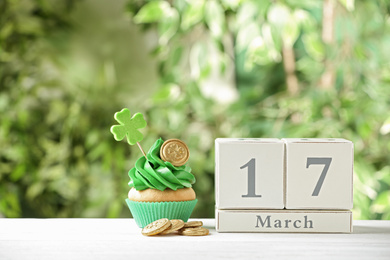 Photo of Composition with block calendar on white wooden table against blurred greenery. St. Patrick's Day celebration