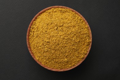 Wooden bowl with turmeric powder on dark background, top view