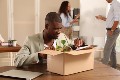 Photo of New coworker unpacking box with personal items at workplace in office
