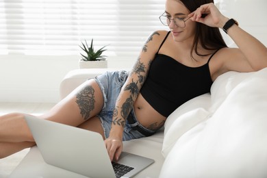 Beautiful woman with tattoos on body using laptop in living room