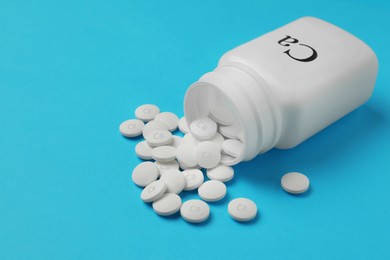 Overturned bottle of calcium supplement pills on light blue background, space for text