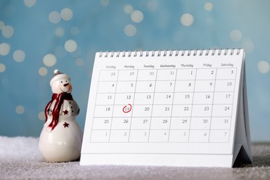 Saint Nicholas Day. Calendar with marked date December 19 and snowman figure on table against blurred lights