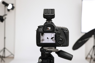 Photo of Tripod with camera, bar stool and professional lighting equipment in modern photo studio, focus on screen