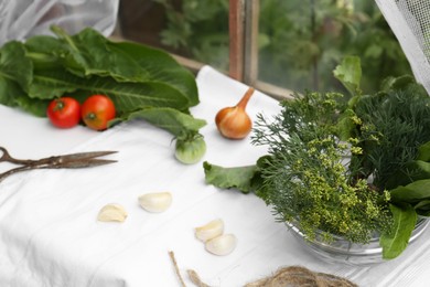 Fresh green herbs, tomatoes, garlic cloves and onion on table indoors