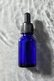 Bottle of face serum in water on light background, top view
