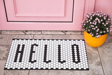 Stylish door mat with word HELLO and beautiful flowers near entrance