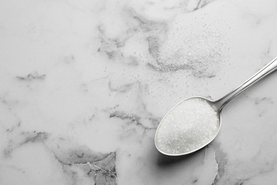 Spoon of white sugar on marble table, top view. Space for text