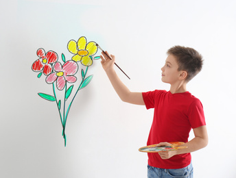 Little boy drawing flowers on white wall 
