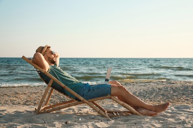 Man with laptop relaxing in deck chair on beach