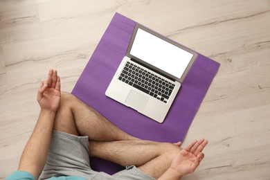 Photo of Man practicing yoga while watching online class at home during coronavirus pandemic, top view. Social distancing