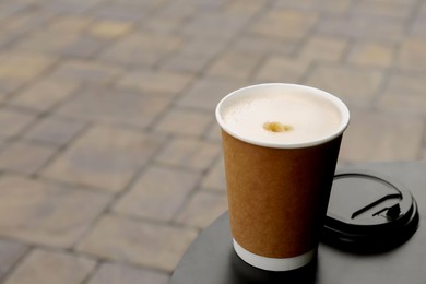 Cardboard cup with plastic lid on black table outdoors, space for text. Coffee to go