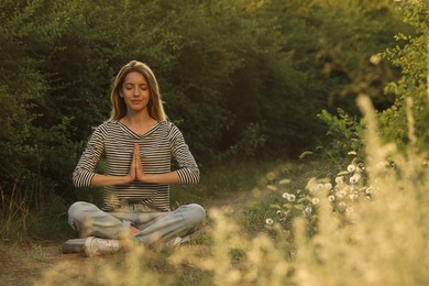 Photo of Young woman meditating on green grass outdoors, space for text