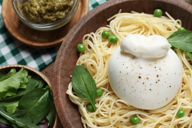 Photo of Bowl of delicious pasta with burrata, peas and spinach served on table, flat lay
