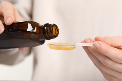 Photo of Woman pouring syrup from bottle into dosing spoon, closeup. Cold medicine