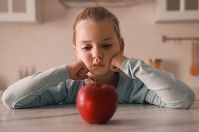 Cute little girl refusing to eat apple in kitchen