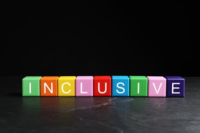Photo of Colorful cubes with word Inclusive on marble table against black background. Space for text