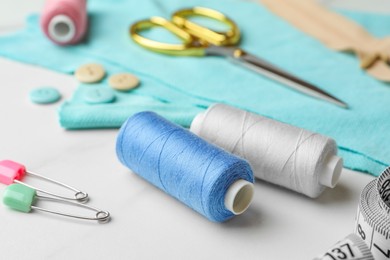 Threads and other sewing supplies on white marble table, closeup