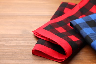 Folded red and blue checkered bandanas on wooden table, space for text