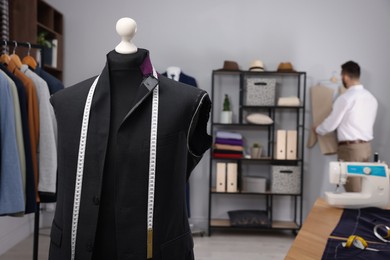 Tailor working in atelier, focus on mannequin with unfinished suit jacket and measuring tape