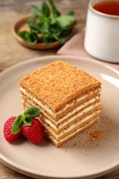 Slice of delicious layered honey cake served with mint and raspberries on plate, closeup