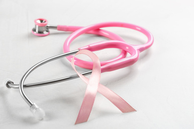 Pink ribbon and stethoscope on light grey stone background, closeup. Breast cancer concept