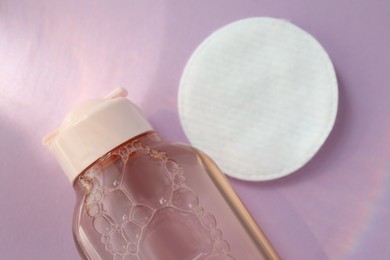 Bottle of micellar water and cotton pad on pink background, closeup