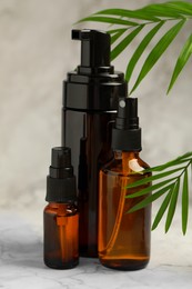 Photo of Bottles of organic cosmetic products and green leaves on light marbled background