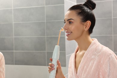 Woman using high frequency darsonval device in bathroom, space for text