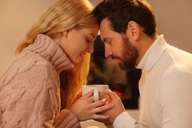 Lovely couple with cup of hot drink spending time together near fireplace at home