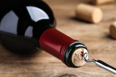 Opening wine bottle with corkscrew on wooden table, closeup